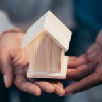 Close-up of hands holding a wooden house model representing real estate or new home purchase.