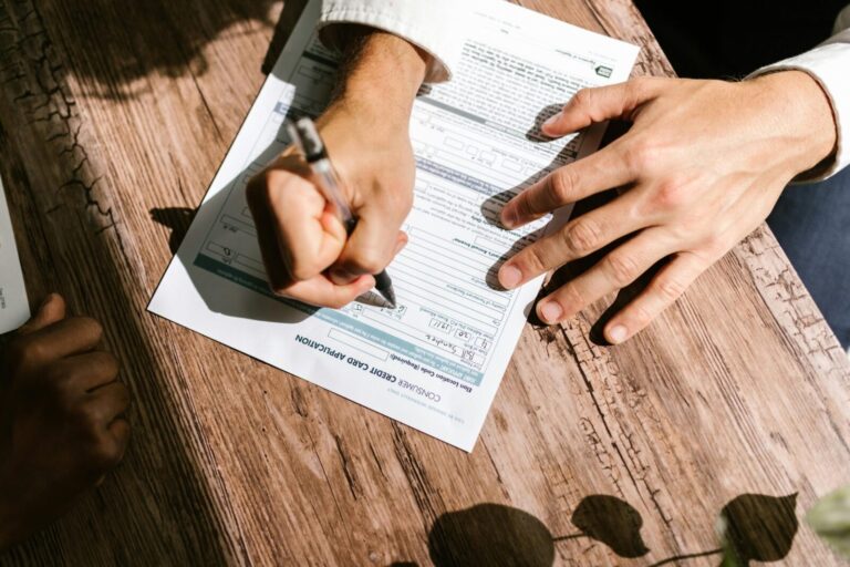 Hands writing on a consumer loan credit application form on a wooden table.